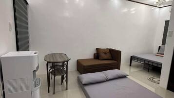 A modern room with a bed, a sofa, a table, and a refrigerator.