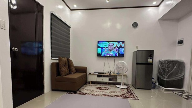 Een moderne woonkamer met een bank, een flatscreen-televisie, een ventilator, een koelkast en een schuifdeur.