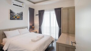 A hotel room with a bed, a desk, an air conditioner, a painting, and a window with curtains. - Orchid Paradise Homes OPV513 (Hin Lek Fai)
