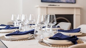 Una mesa de comedor dispuesta con varias copas de vino, platos y cubiertos, con una chimenea al fondo.