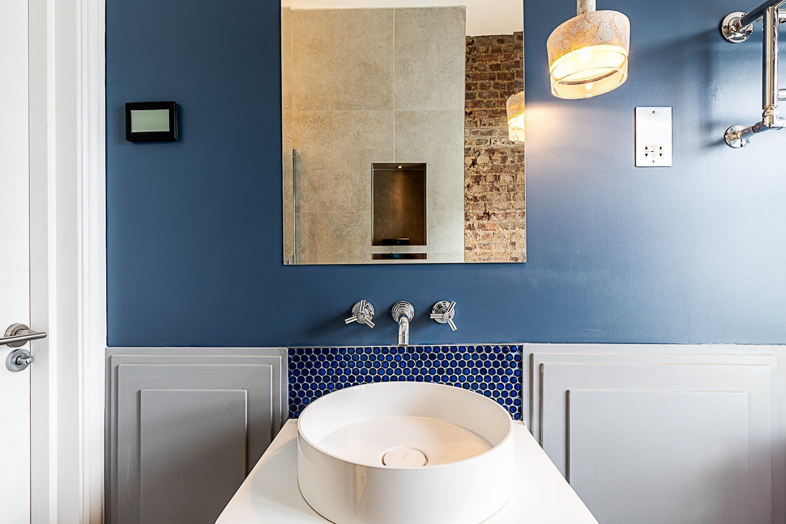 Un baño con pared azul, un lavamanos blanco, un espejo y una lámpara colgante.