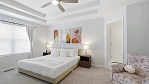 Un dormitorio con una cama, ventilador de techo, cuadros en la pared y una silla.