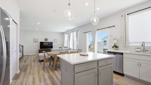 Cocina moderna con una isla central, un comedor con televisor y vistas al exterior.