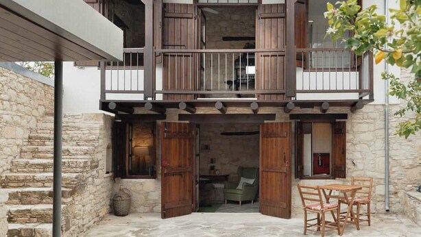 Un edificio de dos plantas con fachada de piedra, barandillas de balcón de madera y una escalera de piedra que conduce al nivel superior.