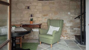 Una habitación con paredes de piedra, un sillón verde, una mesita con una planta en maceta y una chimenea.