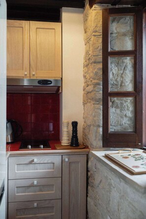 A kitchen with wooden cabinets, a red tiled backsplash, a stone wall, and a window with a view.