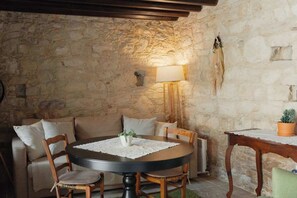 A cozy room with a stone wall, a round table with chairs, a sofa, a lamp, and a small table with a plant.