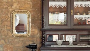 A wooden cabinet with glass doors, a mirror, and a chair against a stone wall. - Traditional Stone Studio Village Retreat (Potamiou)