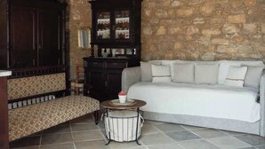 A room with a stone wall, a dark wooden cabinet, a white sofa, a patterned bench, and a small round table with a flower vase. - Traditional Stone Studio Village Retreat (Potamiou)