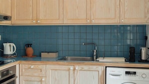 A kitchen with wooden cabinets, a blue tiled backsplash, a Bosch dishwasher, and a coffee maker. - Traditional Stone Studio Village Retreat (Potamiou)