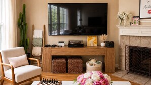 A living room with a television, a fireplace, a chessboard, and a vase of flowers. - Pool, Hot Tub, Huge Outdoor Theater, Mini Golf, Bowling, BBQ, Fire Pit,Sleeps 19 (Pflugerville)