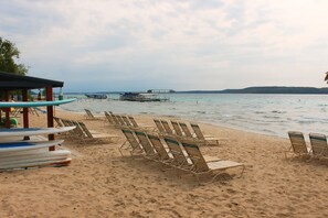 Ein Strand mit Liegestühlen, Surfbrettern und einem Pier im Hintergrund, das Meer ist ruhig.
