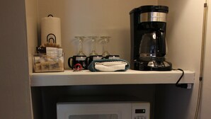 Eine Küchenzeile mit einer Mikrowelle, einem Kühlschrank, einer Kaffeemaschine und einer kleinen Ablagefläche mit Gläsern und einem Handtuch.