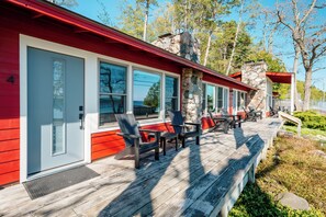 Ein rotes Gebäude mit großen Fenstern, einem Steinkamin und einer Holzterrasse mit Stühlen und einer Bank.