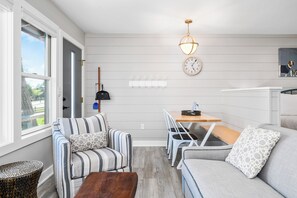 Ein modernes Wohnzimmer mit Sofa, Sesseln, einem Esstisch, einer Uhr und einer Pendelleuchte.