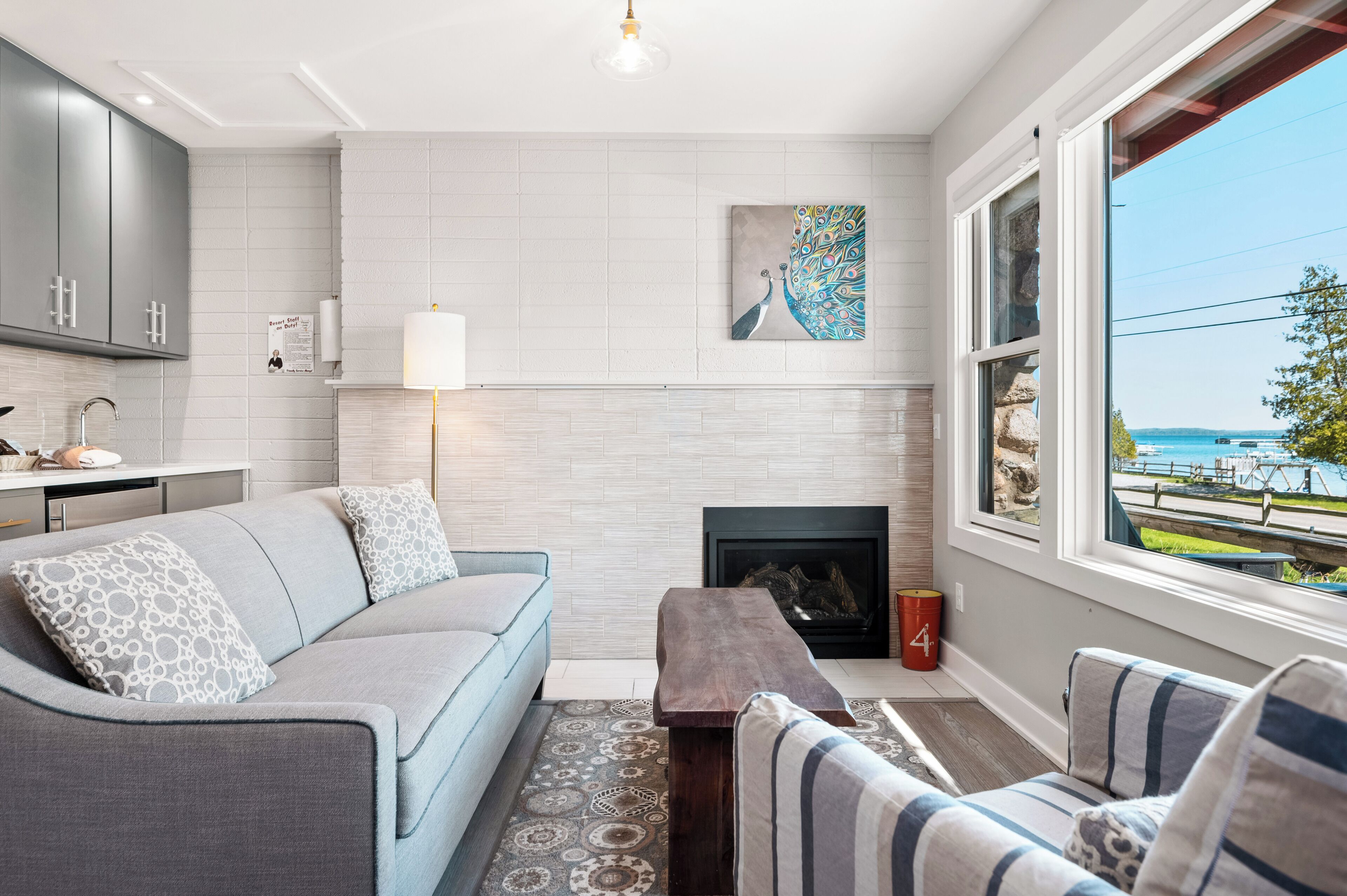 A modern living room with a sofa, a coffee table, a fireplace, and a large window with a view.