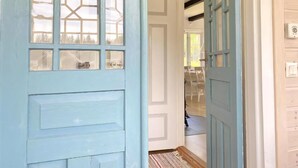 Un pasillo con una puerta azul claro, una puerta blanca y vista a un cuarto con una mesa y sillas de comedor.