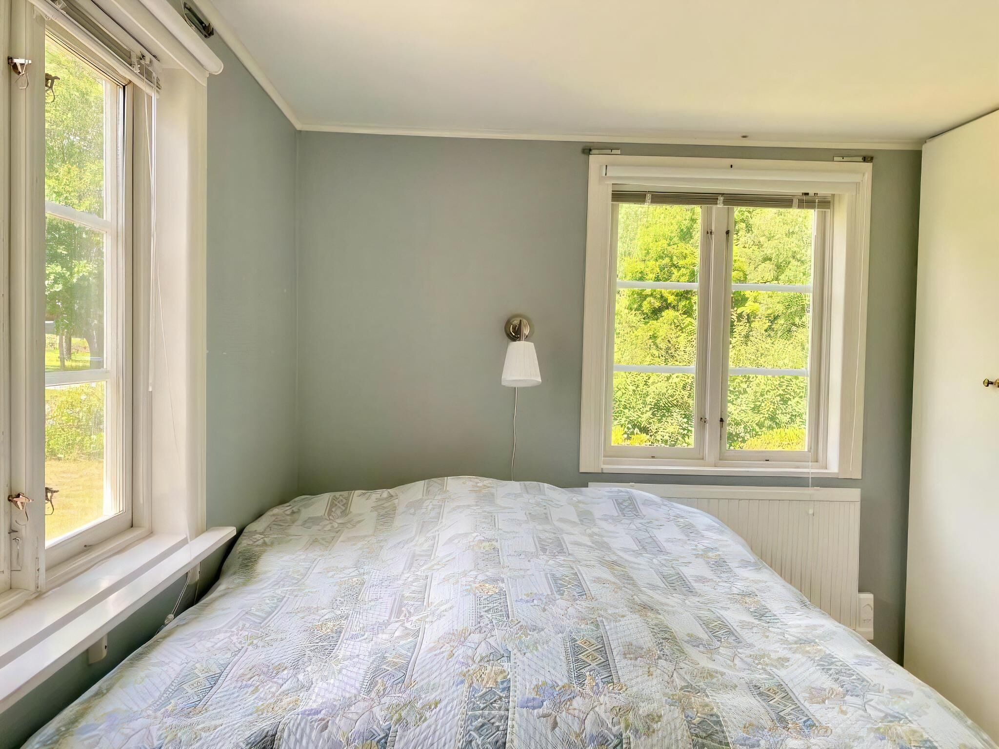 Une chambre à coucher avec un lit, une fenêtre et une lampe fixée au mur.