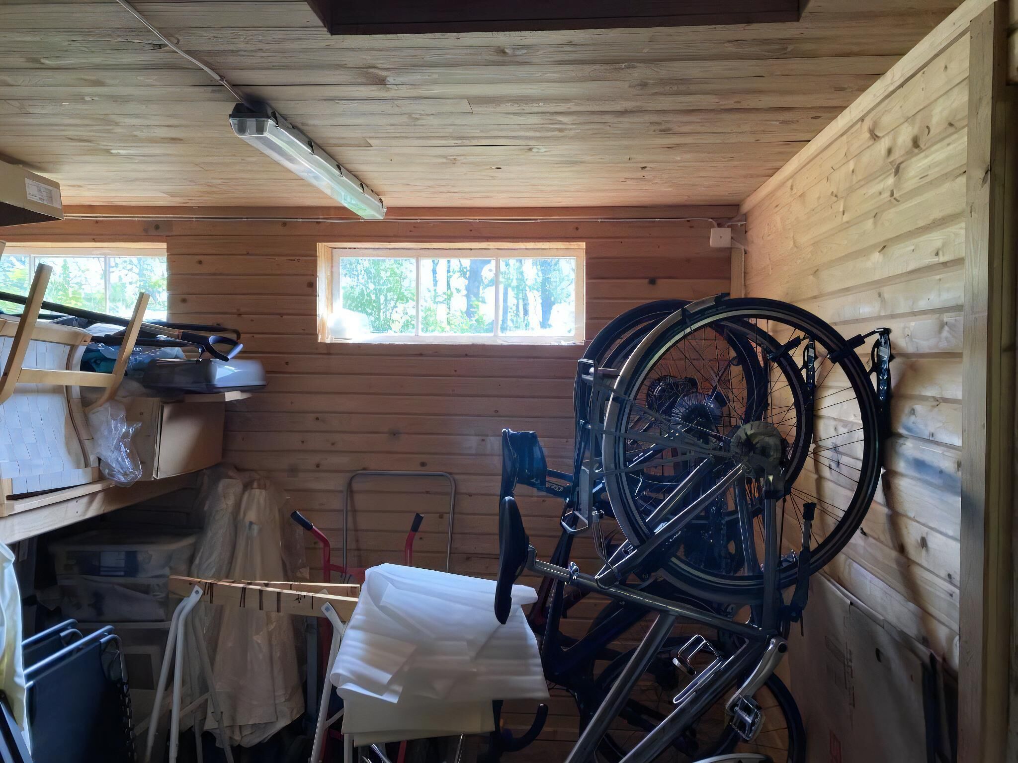 Een houten blokhutinterieur met een fietsenrek, een raam met uitzicht op bomen en een plafondventilator.