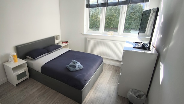 Un dormitorio con cama, mesita de noche, lámpara y ventana con vistas al verdor.