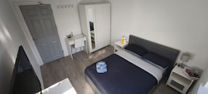 A bedroom with a bed, a desk, a wardrobe, and a nightstand with a lamp and books. - Room-delightful Double Room in Shared Ho (Chelmsford)