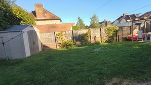 Un patio trasero residencial con un cobertizo, cerca de madera y un área de patio con sillas y una mesa.