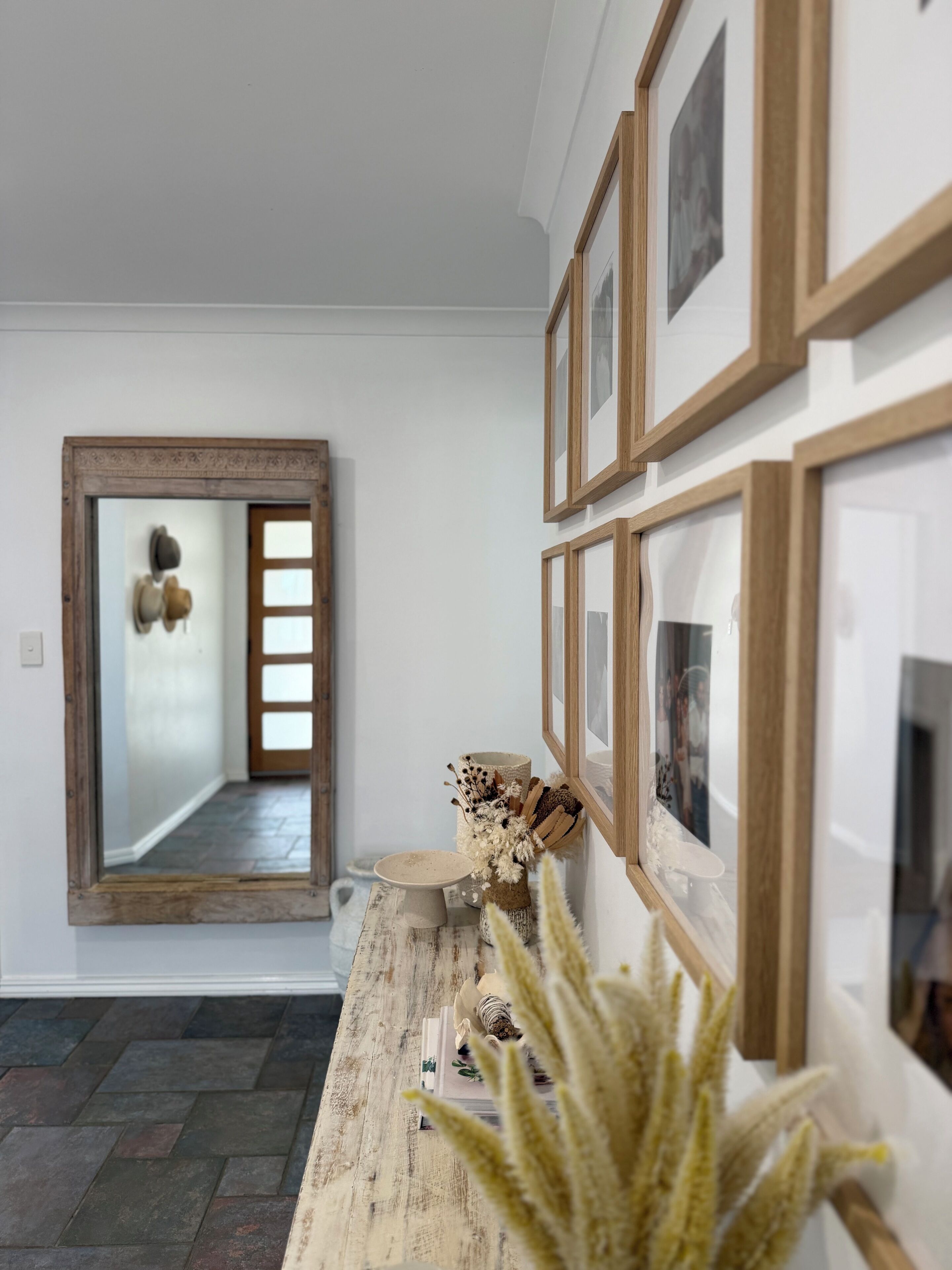 A hallway with a wooden door, a mirror, and a wall with framed pictures.