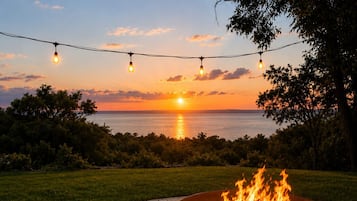 A person sitting by a fire pit with a sunset view.