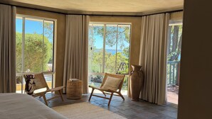 A bedroom with a large bed, two wicker chairs, a large vase, and a view of greenery and a body of water through large windows. - Private Estuary Retreat | Pool & Sunrise Views - 1.5hrs from Perth (Herron)