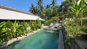 A swimming pool with lounge chairs, surrounded by tropical plants and palm trees. - Salty Cabin Sunset Views Yeh Leh Beach (Selemadeg)