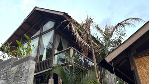 A modern building with large windows, a balcony, and surrounding tropical vegetation. - Salty Cabin Sunset Views Yeh Leh Beach (Selemadeg)