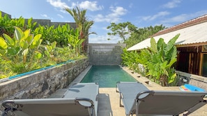 A swimming pool with lounge chairs, surrounded by tropical plants and a stone wall.