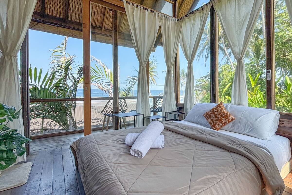 Una habitación con cama, cortinas y vista al mar.