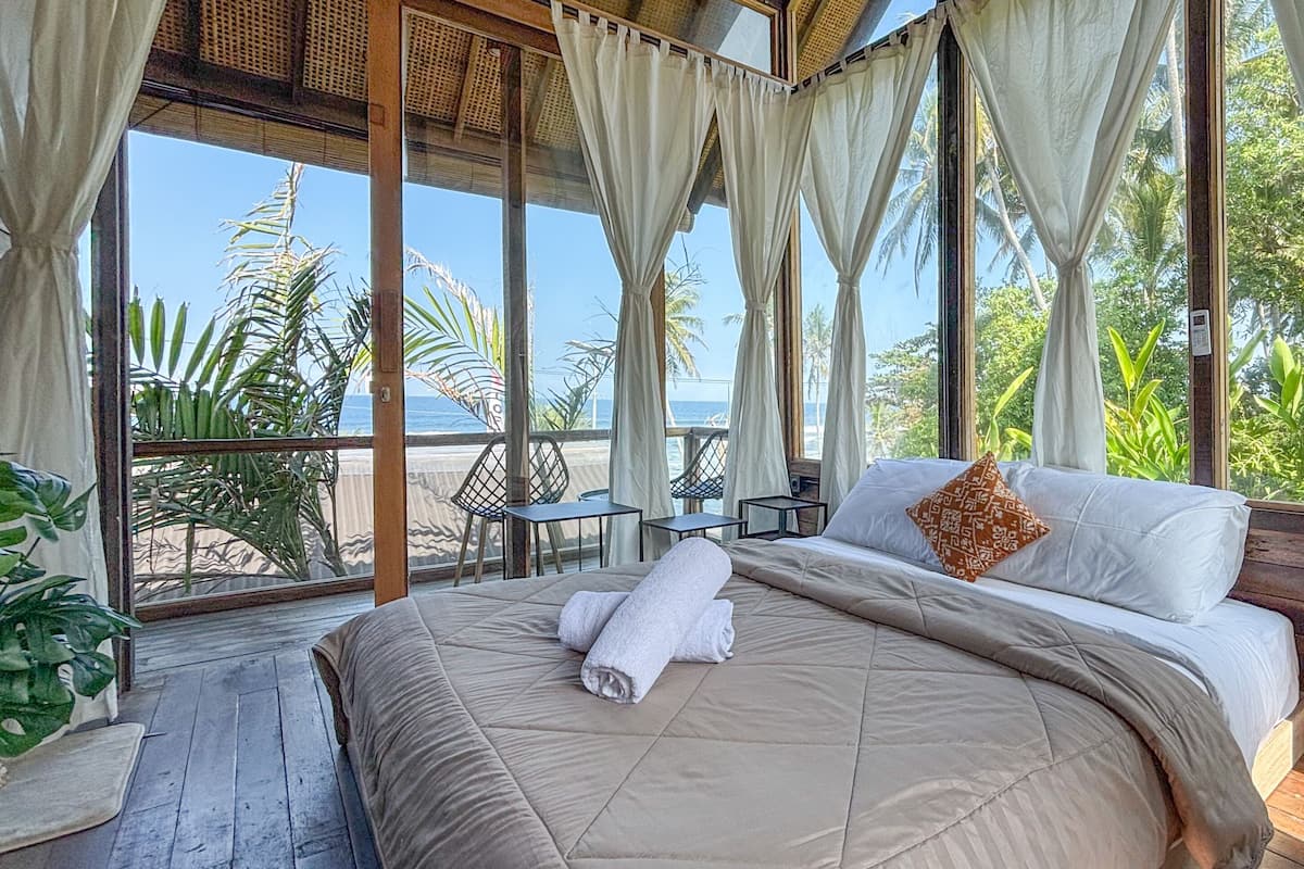 A room with a bed, curtains, and a view of the sea.