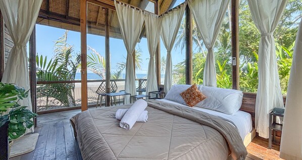 A room with a bed, curtains, and a view of the sea. - Salty Cabin Sunset Views Yeh Leh Beach (Selemadeg)