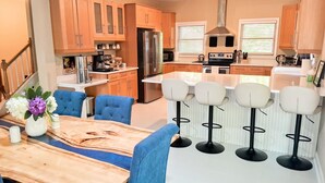 A modern kitchen with wooden cabinets, a stainless steel refrigerator, a built-in oven, and a bar area with stools. - •LAST MINUTE DISCOUNTS• 6BR Epic Views + BBQ + Fully Stocked Kitchen• (Boone)