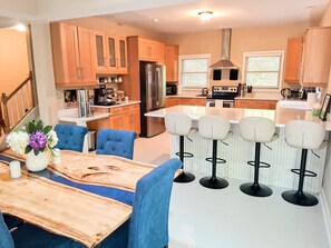 A modern kitchen with wooden cabinets, a stainless steel refrigerator, a built-in oven, and a bar area with stools.