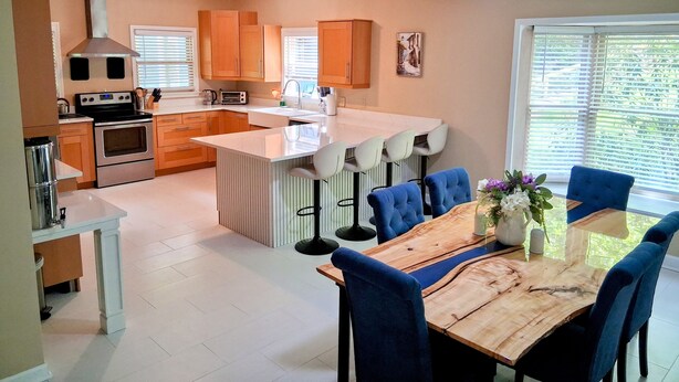 A modern kitchen with a central island, a dining area with blue chairs, and a ceiling fan. - •LAST MINUTE DISCOUNTS• 6BR Epic Views + BBQ + Fully Stocked Kitchen• (Boone)