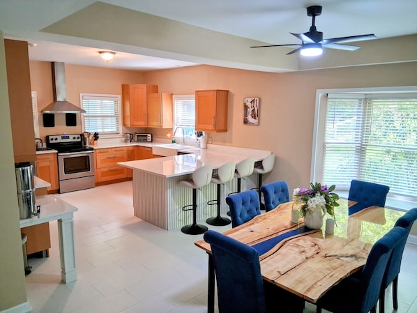 A modern kitchen with a central island, a dining area with blue chairs, and a ceiling fan.