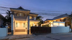 A modern house with a gated entrance, a covered porch, and a well-lit interior. - Grand Hill Mansion (Hua Hin)