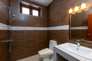 Une salle de bain avec des murs en bois, un lavabo blanc, des toilettes et une douche.