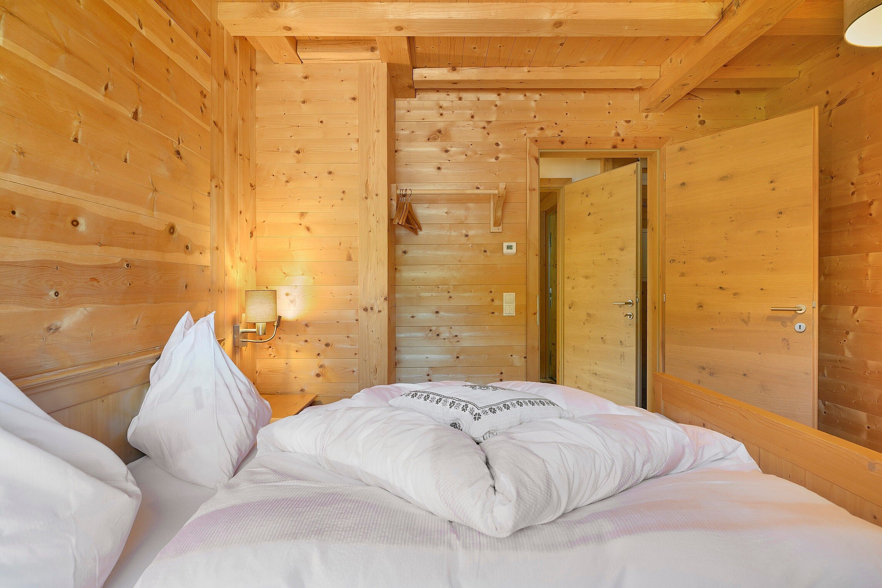 Ein holzgetäfeltes Zimmer im Blockhausstil mit einem Bett, einer Wandleuchte und einer Tür.