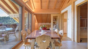 Un comedor de madera con una mesa, sillas, una pared de vidrio y vistas al exterior.