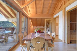 A wooden dining area with a table and chairs, a glass wall, and a view of the outdoors.