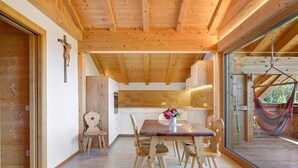Interior de madera con una mesa de comedor, sillas, una cruz en la pared y una hamaca afuera.