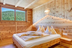 A wooden cabin bedroom with a bed, pillows, a nightstand, a window, and a wall-mounted light.