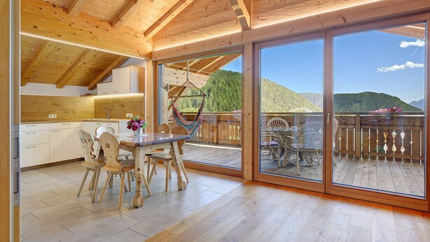 Un interior de madera con comedor, cocina y grandes puertas corredizas de vidrio que dan a una terraza exterior.