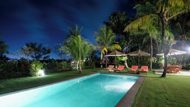 A swimming pool with lounge chairs and umbrellas, surrounded by palm trees and a well-maintained lawn. - Dream View Villa - 5 Br (Pecatu)