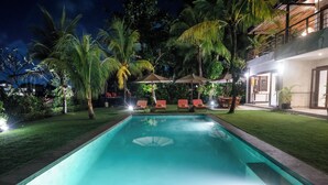 A swimming pool with lounge chairs and umbrellas, surrounded by palm trees and a well-maintained lawn. - Dream View Villa - 5 Br (Pecatu)