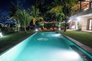 A swimming pool with lounge chairs and umbrellas, surrounded by palm trees and a well-maintained lawn. - Dream View Villa - 5 Br (Pecatu)